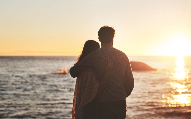 Pareja abrazada viendo el atardecer en la playa