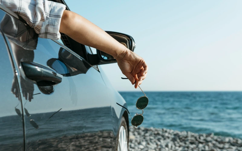 Mujer con la mano fuera de la ventanilla del coche junto al mar
