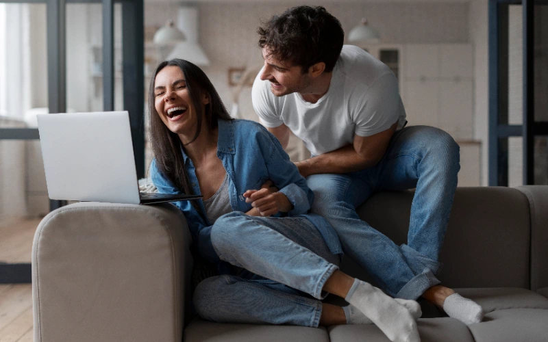 Pareja riendo mientras usa el portátil en el sofá